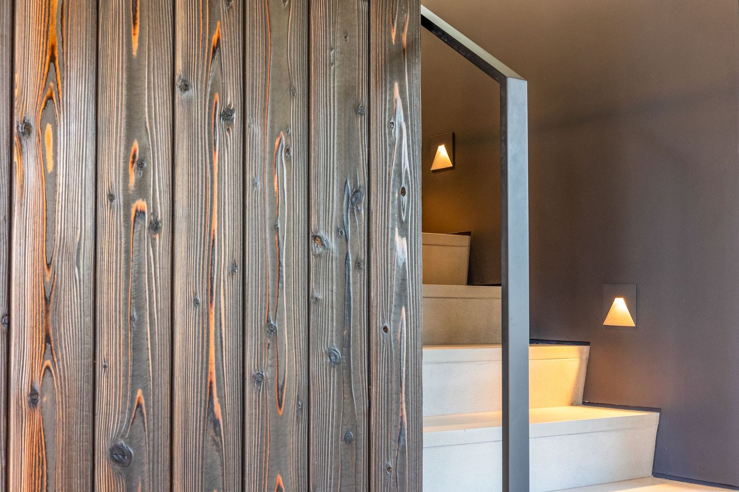Modern interior stairwell with rustic wooden wall paneling and warm sconce lighting creating an inviting atmosphere.