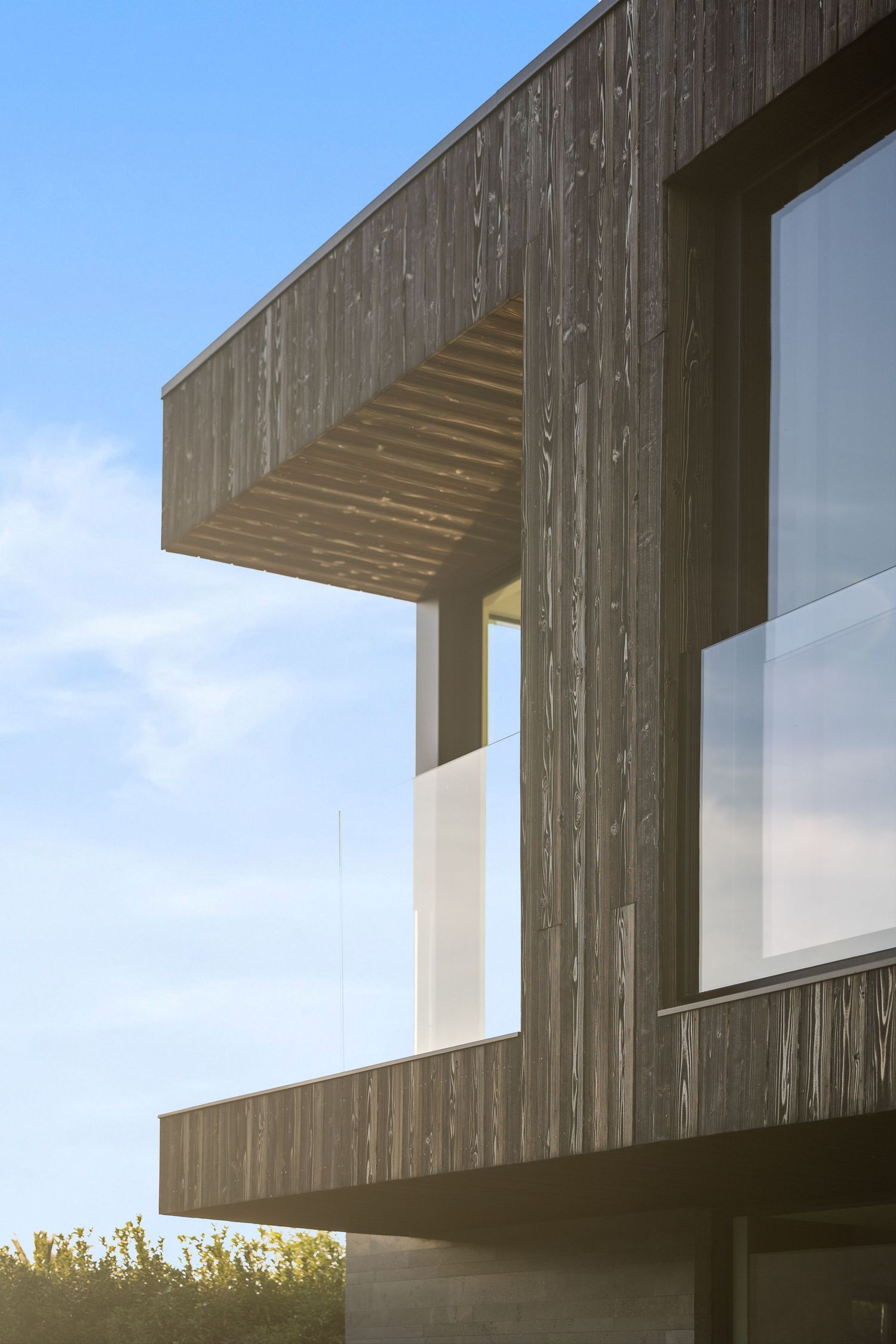 Modern wooden house exterior with cantilevered balcony and large windows against blue sky in contemporary architectural design.