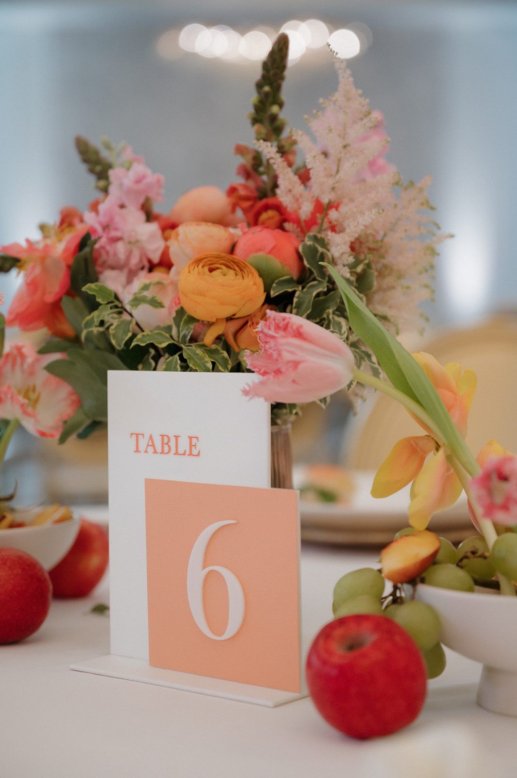 Wedding reception table number 6 card with peach and pink floral centerpiece and red apples as decor elements.