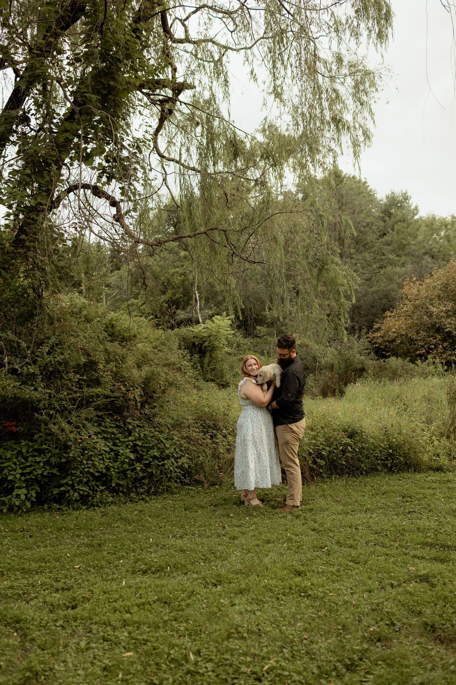 A carefree couple walking with their two dogs on a grassy lawn on a sunny day.