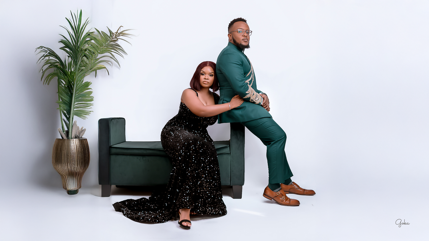 A couple poses together on a green bench against a white backdrop during a professional photoshoot.
