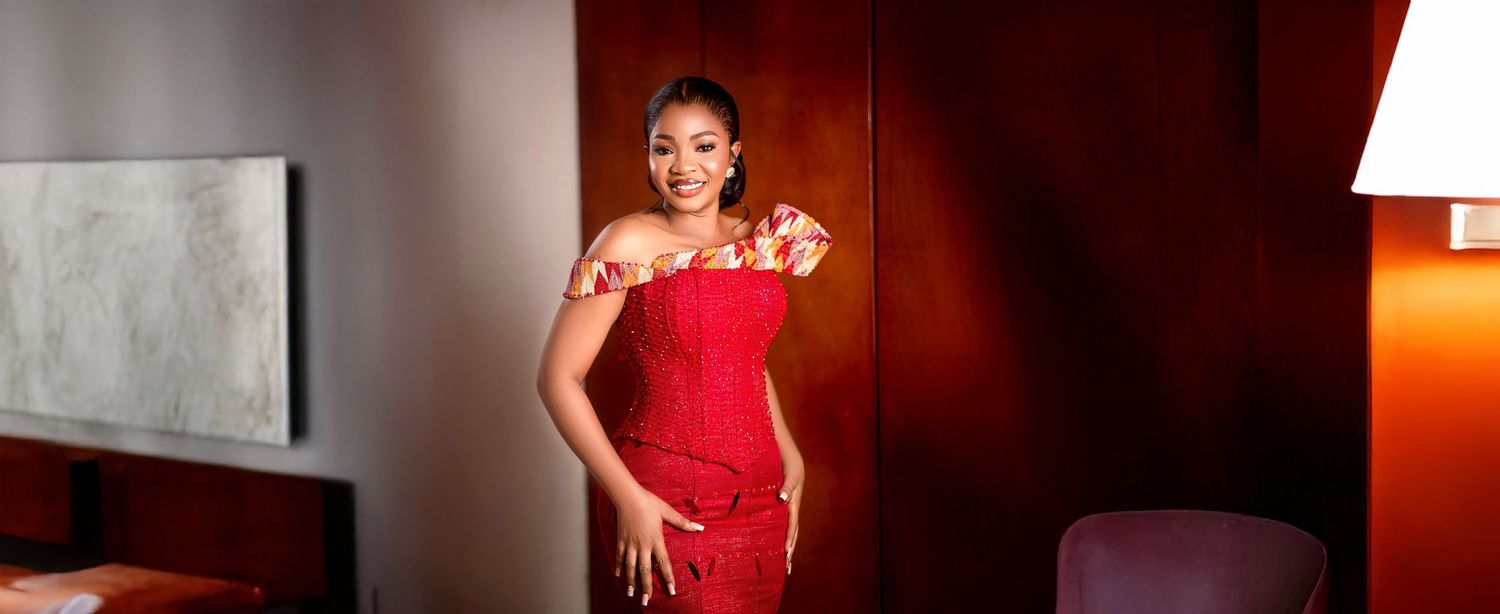 A woman in a vibrant red off-shoulder dress poses elegantly in a luxurious hotel room setting.