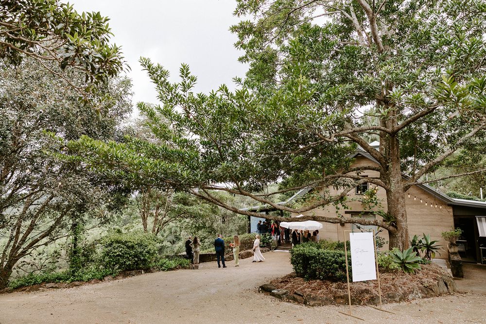 A winding garden path leads through lush trees and landscaping at an outdoor venue with signage.