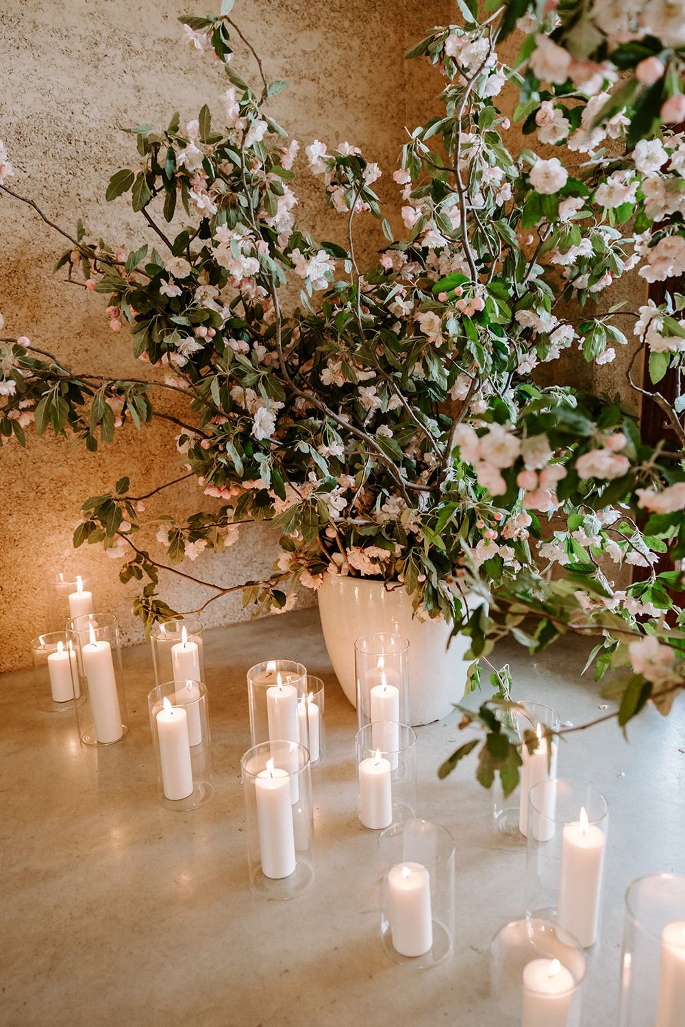 White pillar candles in glass cylinders glow beneath hanging floral arrangements creating an ethereal wedding atmosphere.