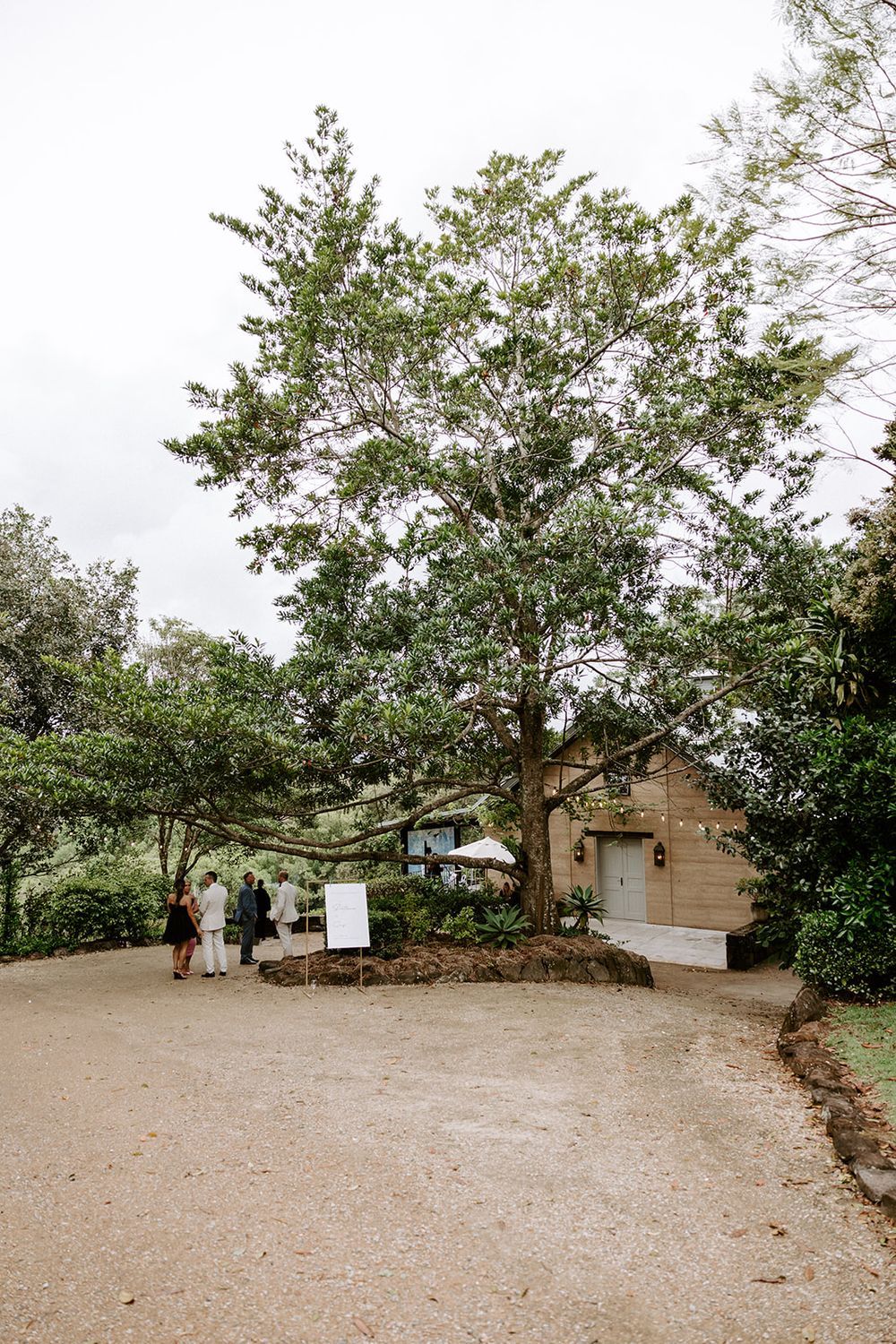 A wide dirt clearing surrounded by trees and small buildings in a natural setting.