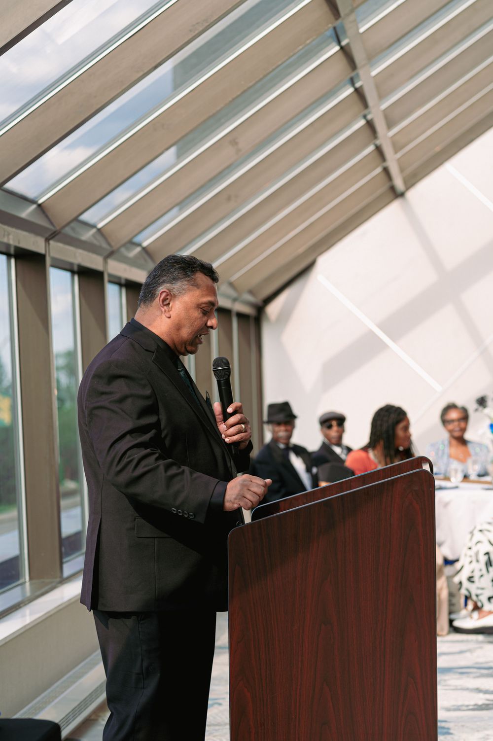 Speaker at podium during formal event in glass-roofed venue.