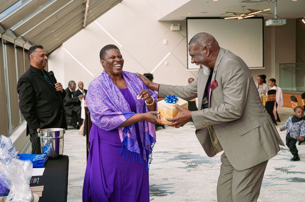 Two people exchanging a gift at a formal event in a sunlit atrium space.