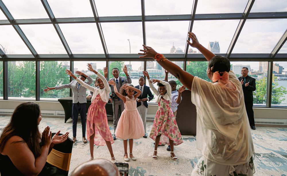 People dancing joyfully in a sunlit room with glass ceiling during a celebration.