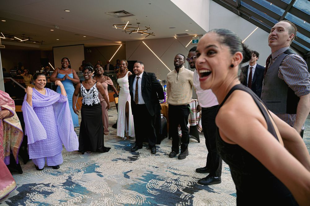 Lively celebration scene with guests dancing and laughing in an elegant glass-roofed venue.