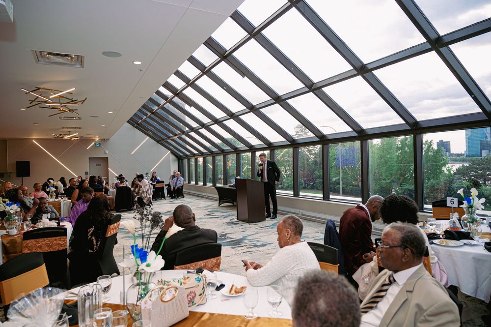 Event gathering in a glass-roofed venue with tables set for dining and guests mingling.