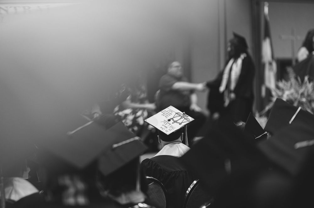 Black and white photo of graduates in caps and gowns during a ceremony.