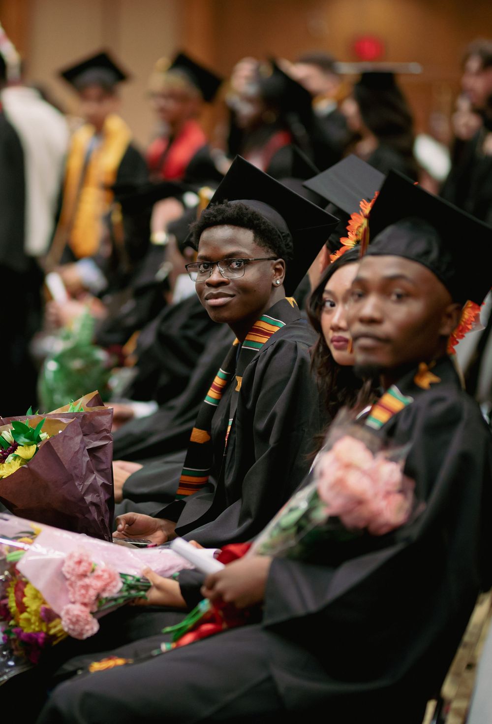 Graduates wearing colorful stoles and holding flowers during commencement ceremony.