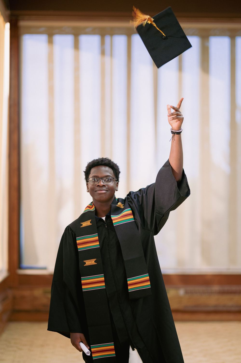 Graduates wearing black robes with colorful kente stoles celebrating their achievement.