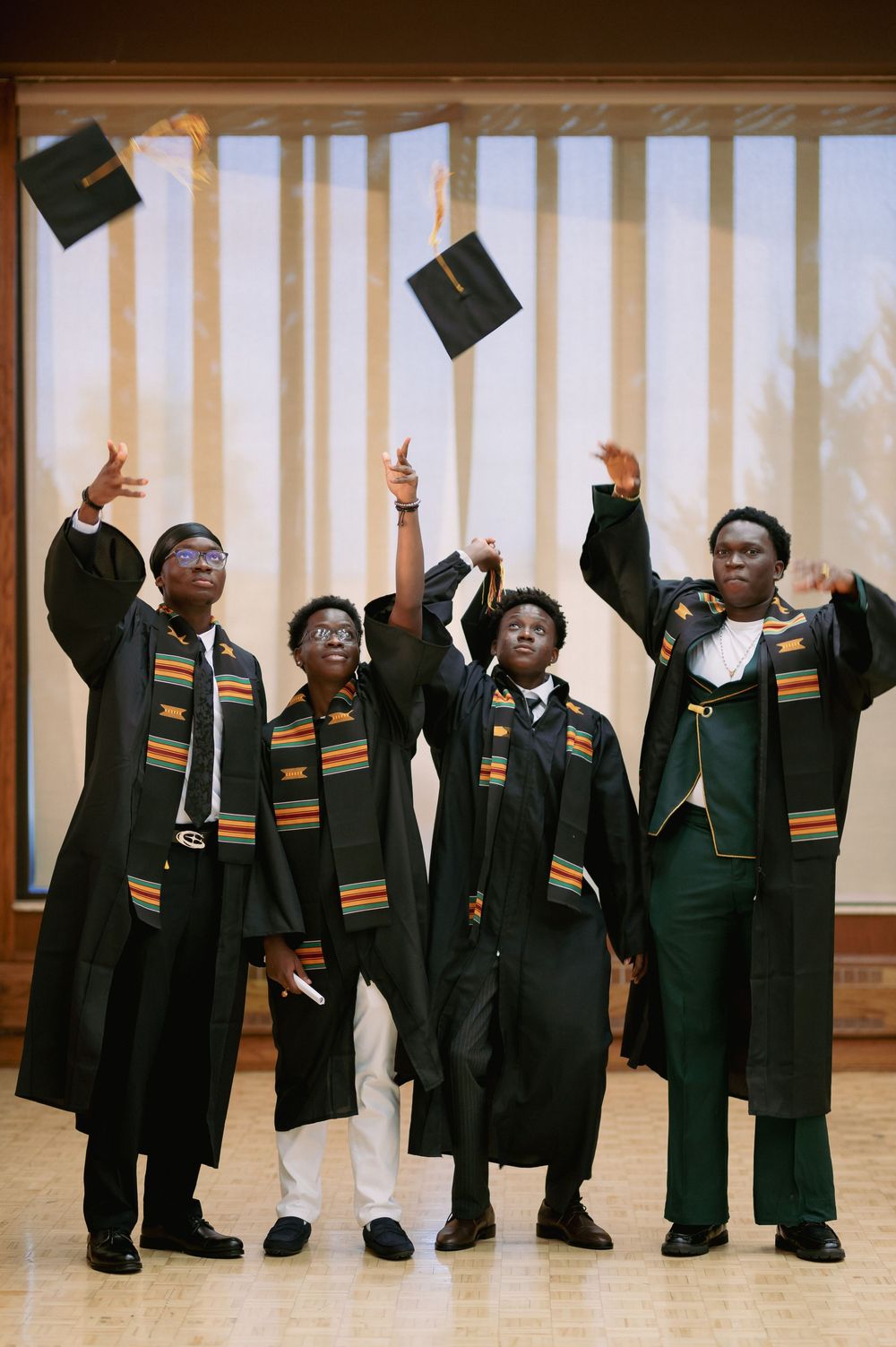 A panoramic shot of graduates in black gowns with kente stoles posing together during commencement.