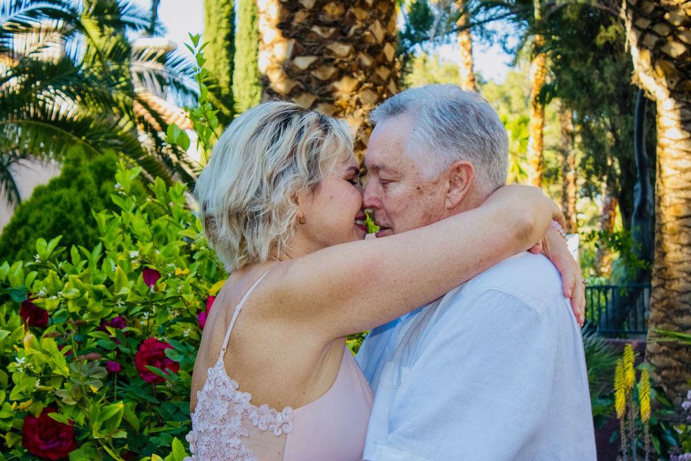 Bride and groom share a romantic kiss during their outdoor tropical garden wedding ceremony with lush palm trees behind them.