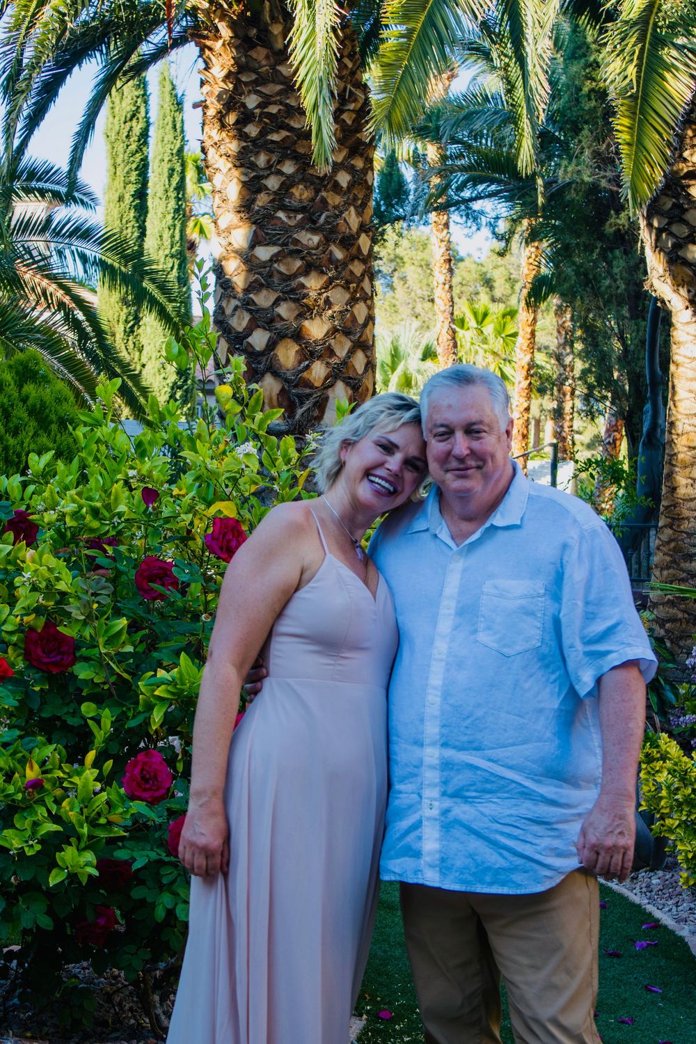 Smiling couple posing together in a lush tropical garden with palm trees and red roses.