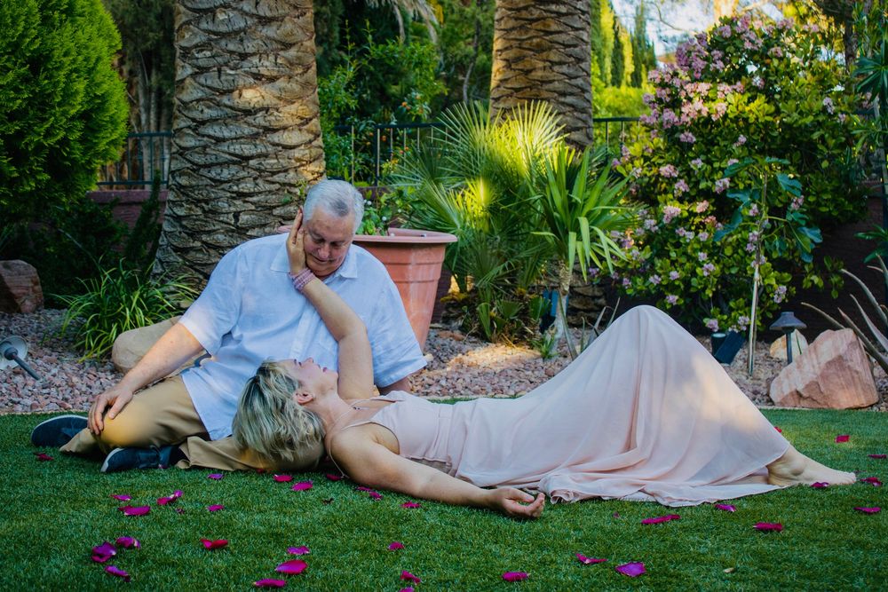 Couple relaxing together on lush green garden lawn surrounded by tropical plants and palm trees.