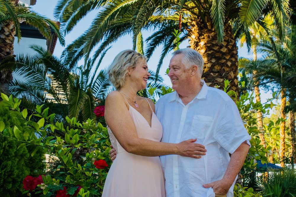 Couple smiling at each other in a tropical garden with palm trees and red flowers.