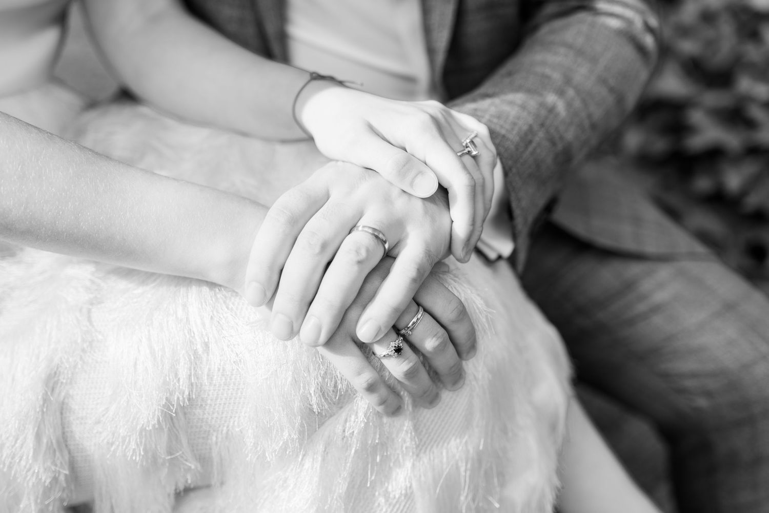 Close-up black and white photo of hands clasped together on white fabric.