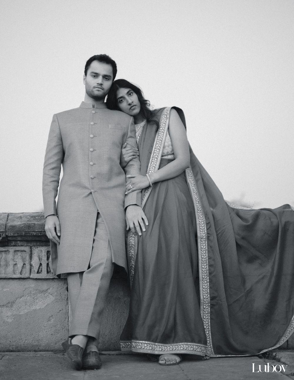 Elegant couple in traditional Indian formal wear posing against white background.