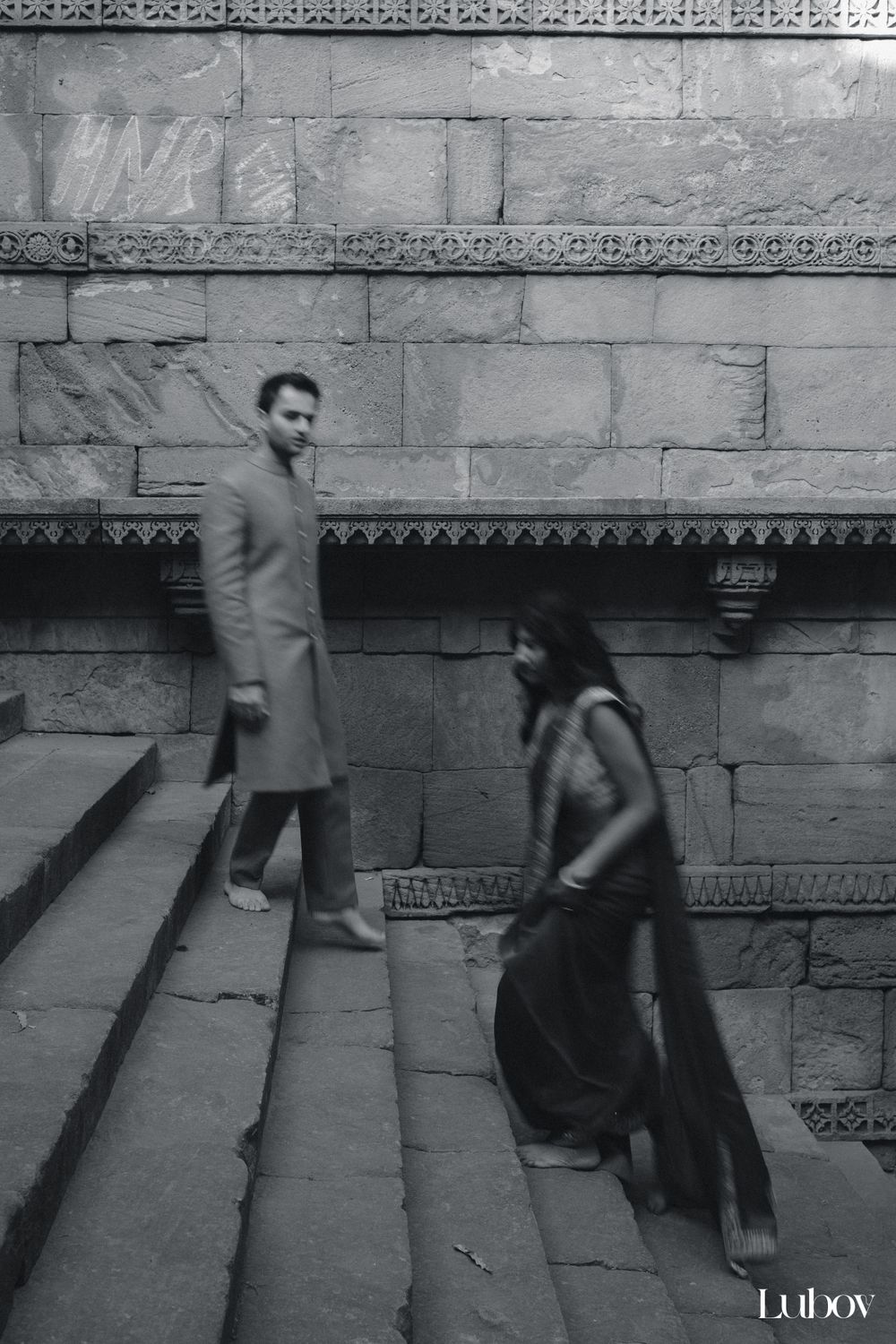 Black and white photo of couple on ornate stone steps with traditional architecture.