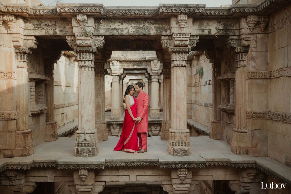 Couple in red attire standing in ancient Indian temple with intricate stone carved pillars.