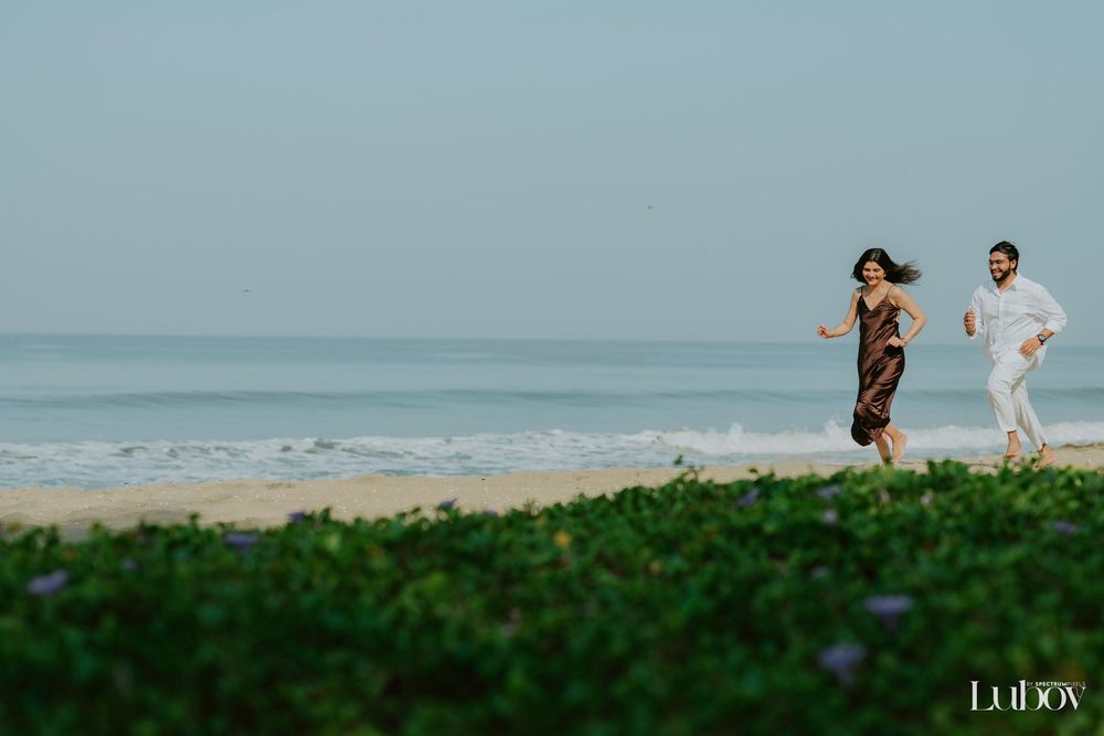 Two people jog together along a scenic beach with green foliage in the foreground and blue ocean waves behind them.