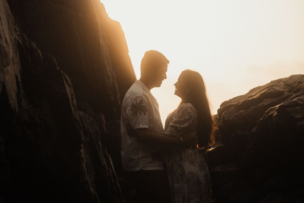 Silhouetted couple sharing intimate moment between rocky cliffs at sunset.