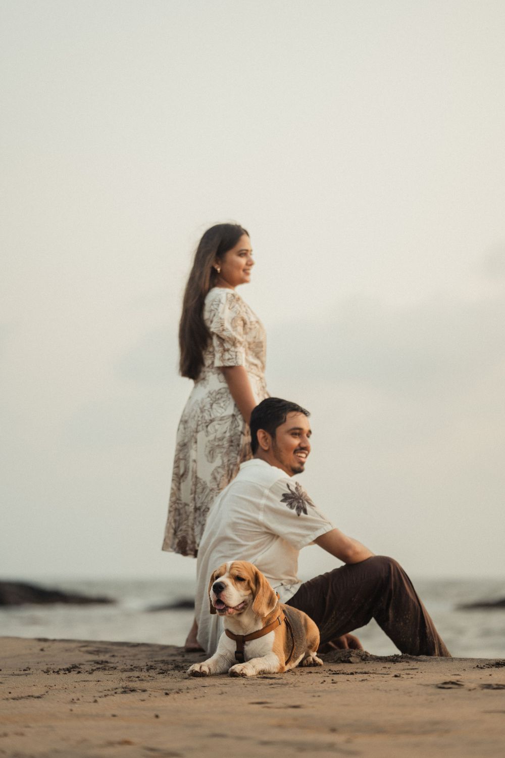 Seaside portrait featuring a couple and their beagle dog sitting on sandy beach.