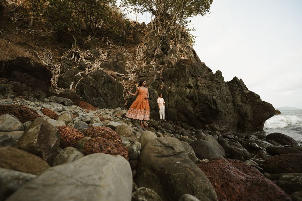 Couple exploring rocky coastal terrain near cliffs with ocean waves in background.