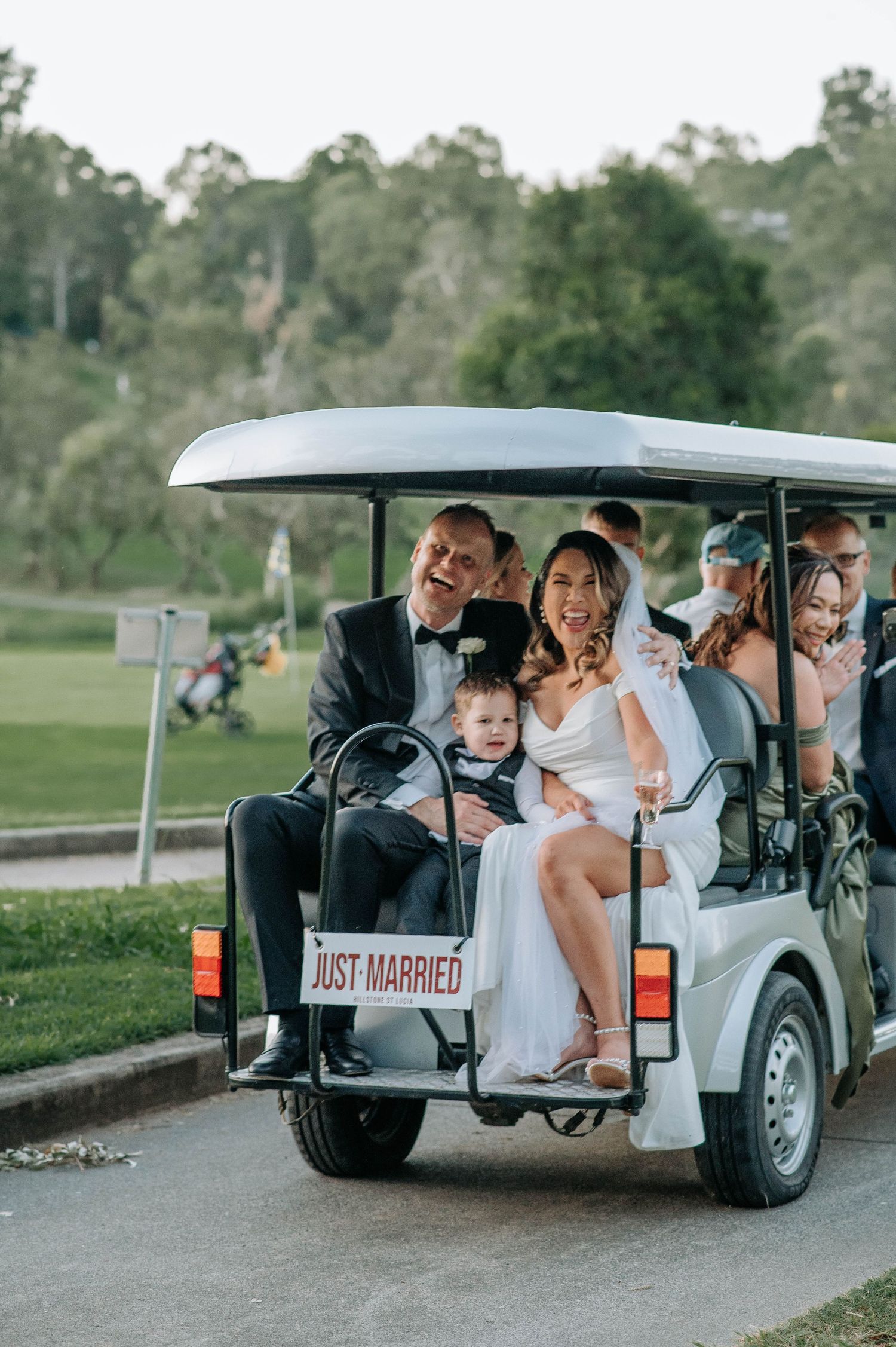 Newlyweds riding in golf cart with 'Just Married' sign through golf course.