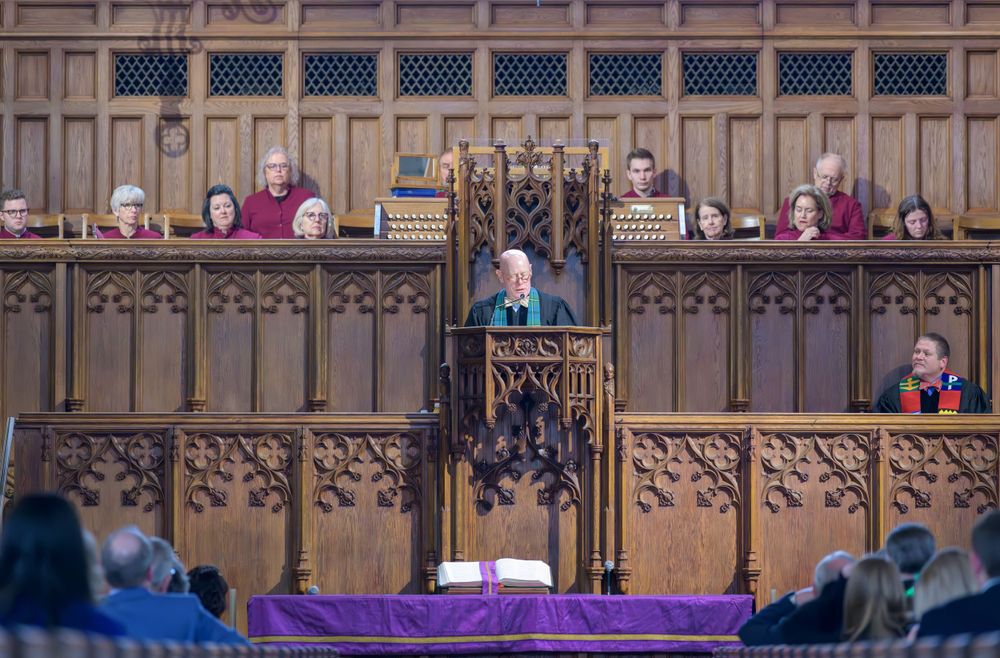 Ornate wooden church choir loft with decorative Gothic details and pews filled with colorful plush toys.