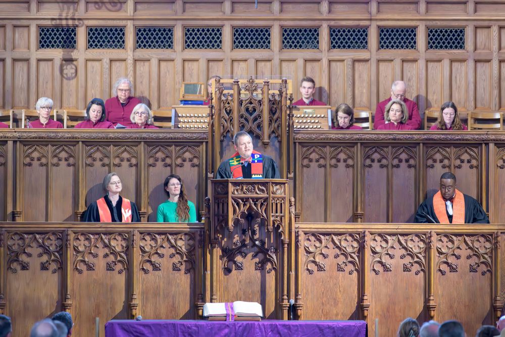 Ornate wooden church pulpit and choir stalls with purple fabric draping the lectern during a religious service.