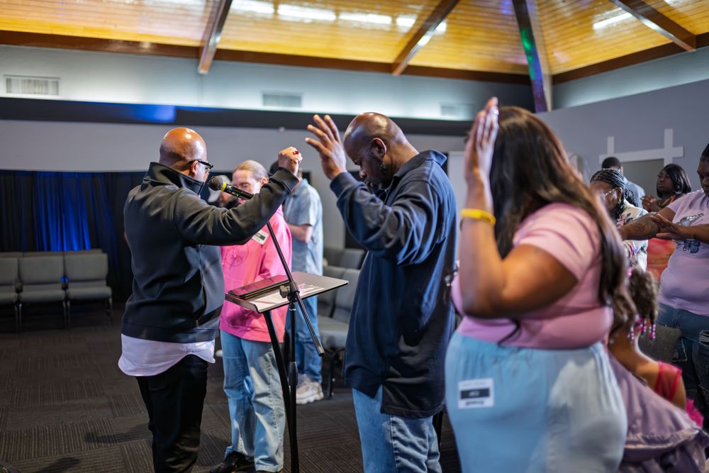 People participating in a prayer laying on of hands ceremony inside a modern church with purple accent lighting.