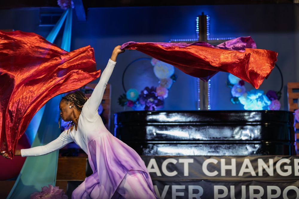 Dancer performs with flowing red fabric on stage at a church event with colorful balloon decorations.