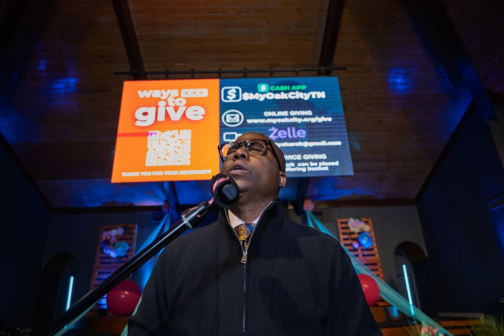 A man speaks at a church podium with a Ways to Give donation screen displayed behind him.