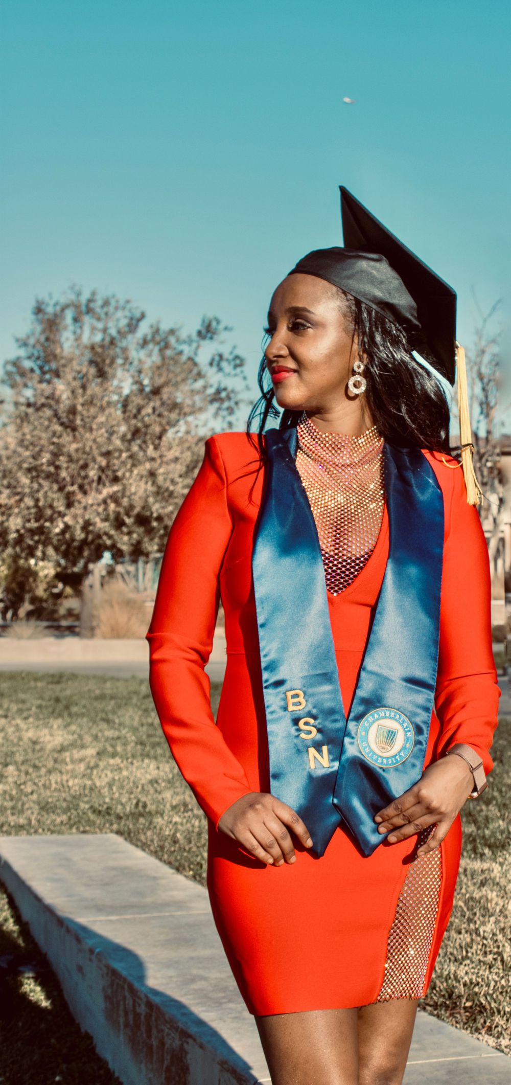BSN nursing graduate in red dress and graduation cap posing confidently in an outdoor setting.