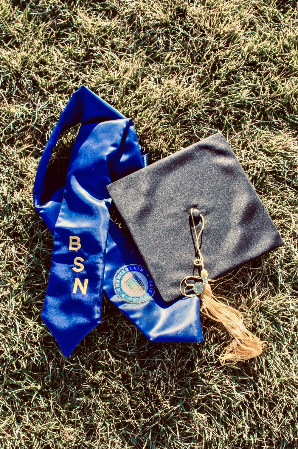 Black graduation mortarboard cap and blue BSN satin stole laid on green grass.