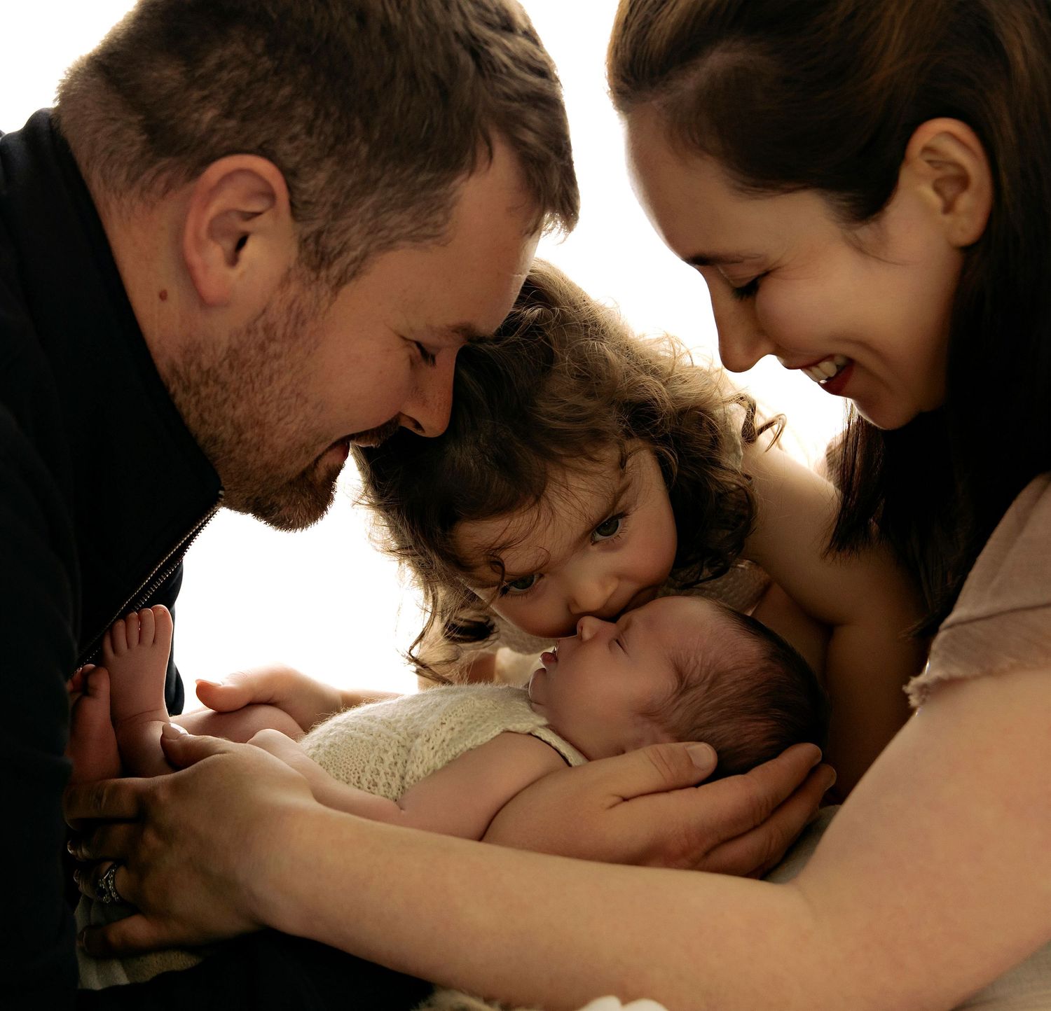 relaxed newborn photographer Westmeath. baby in dads hands, mam, daughter and dad looking over her