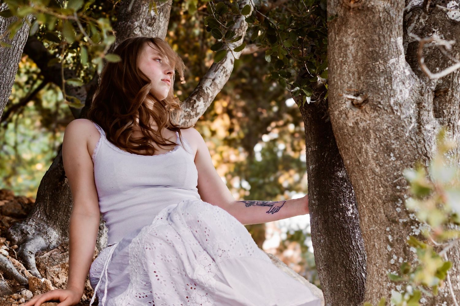 a girl in white sitting in a wooded area.
