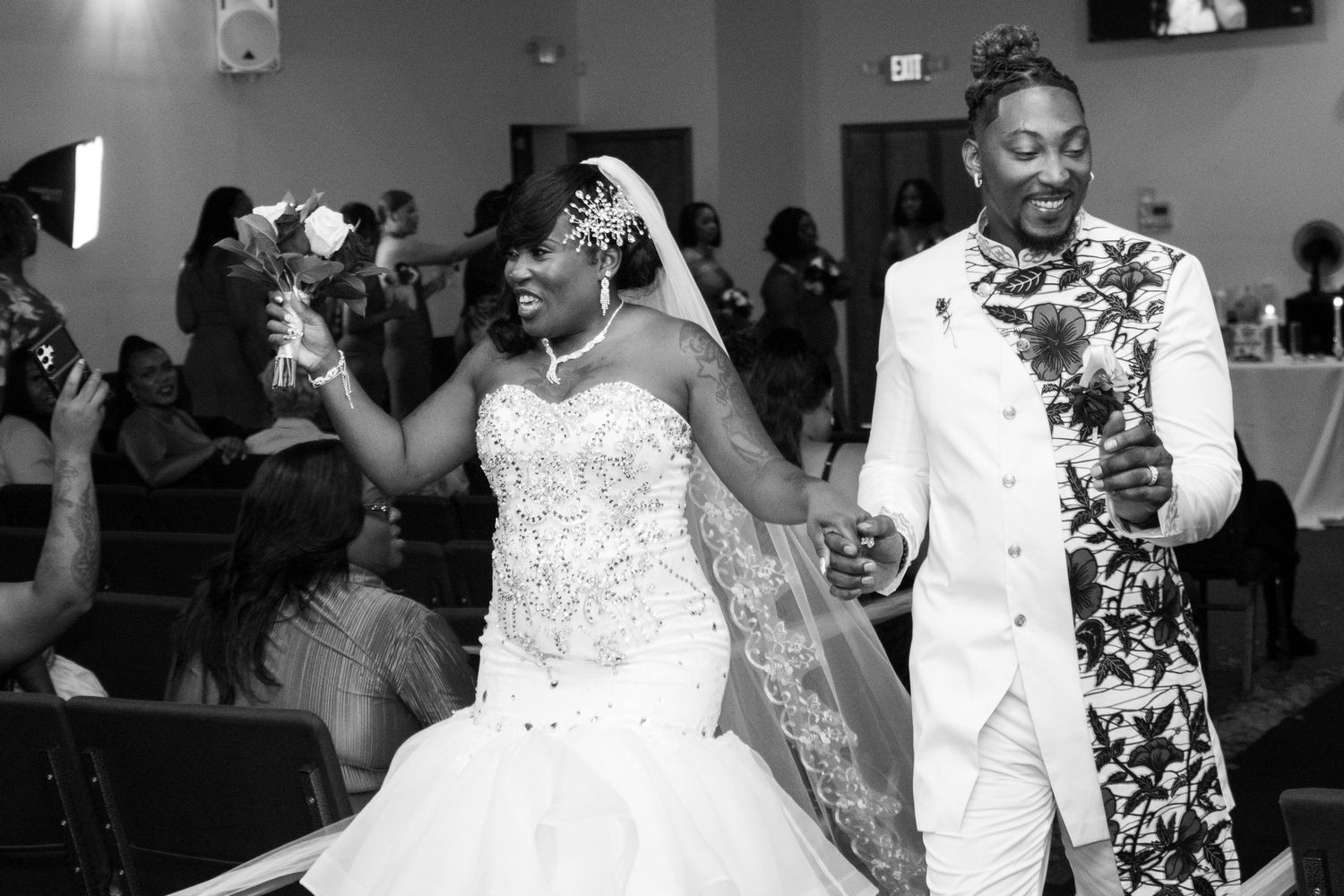 A black-and-white photo of the bride and groom walking down the aisle together, celebrating after the ceremony with flowers in hand.