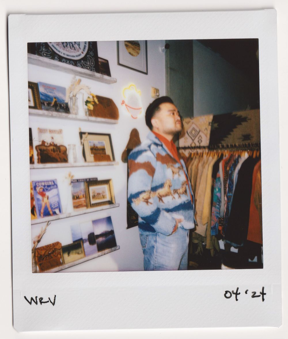 Customer browses vintage clothing section in store with wall displays of photos and artwork.