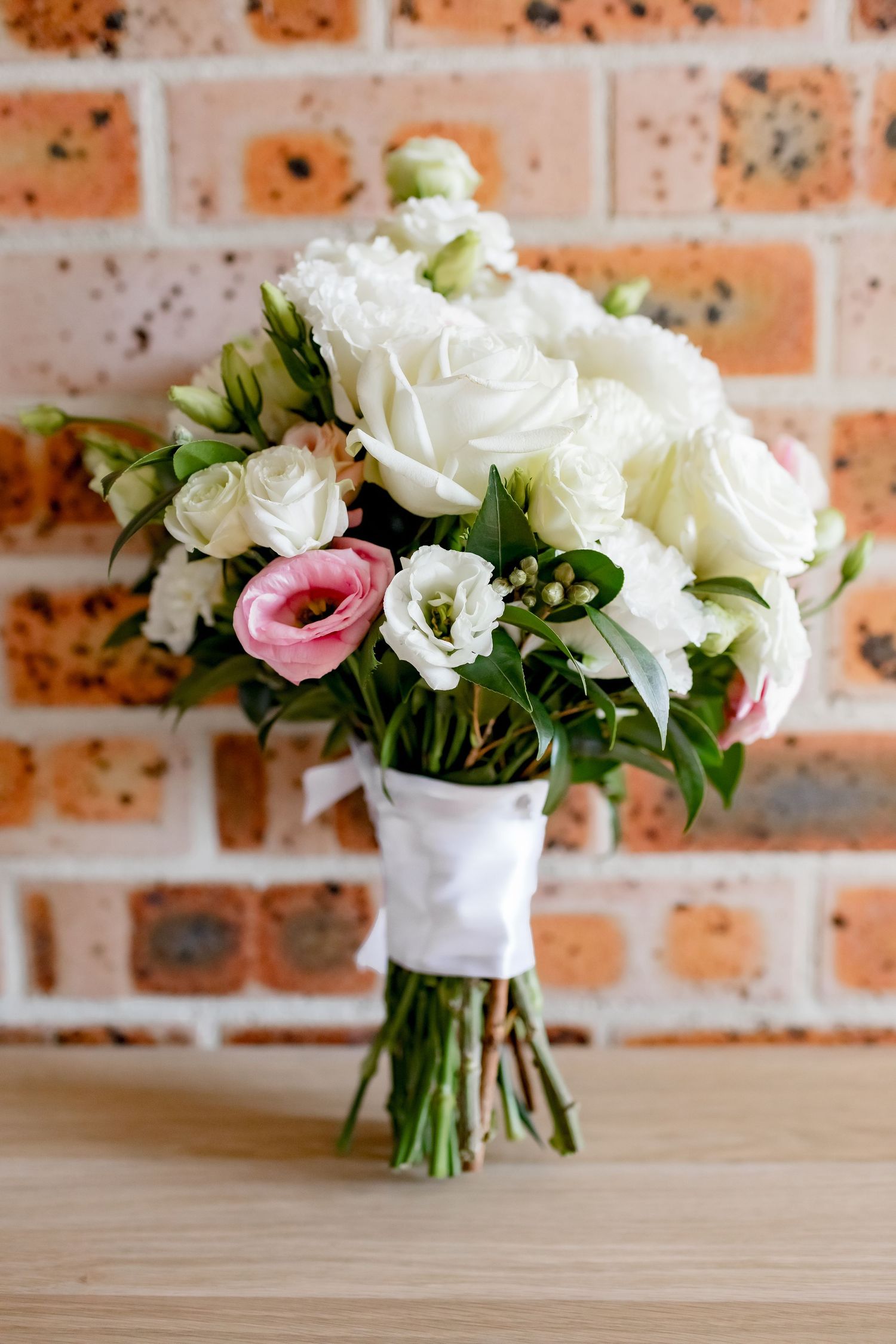 Elegant bridal bouquet of white and pink roses against a brick wall background.