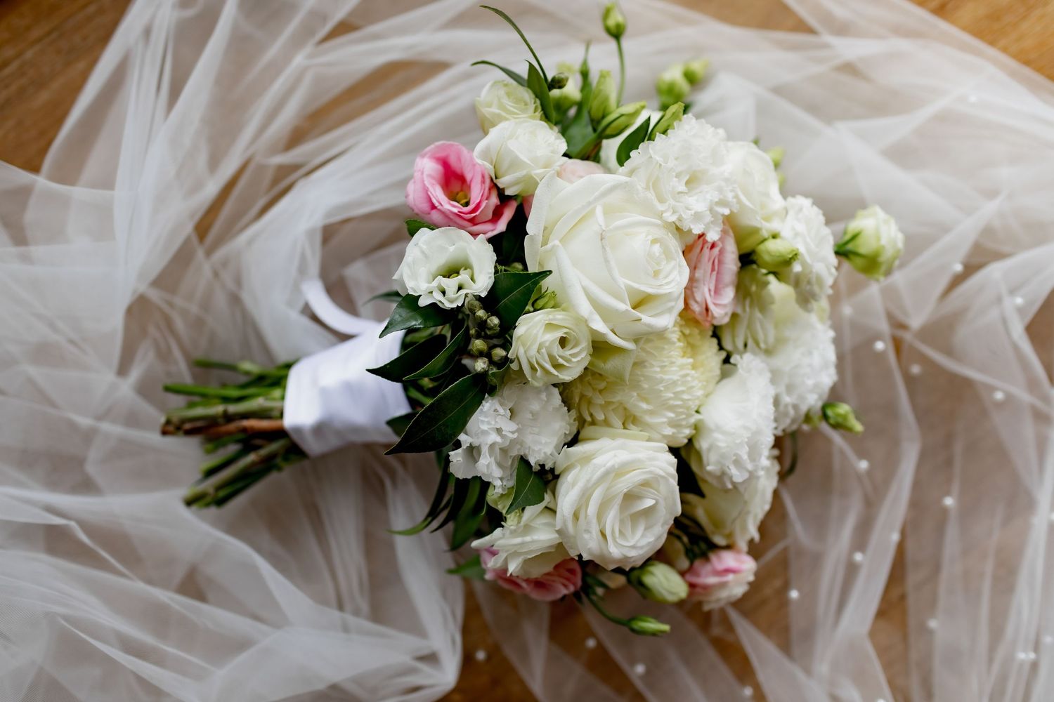 Classic white and pink rose wedding bouquet resting on delicate tulle fabric.