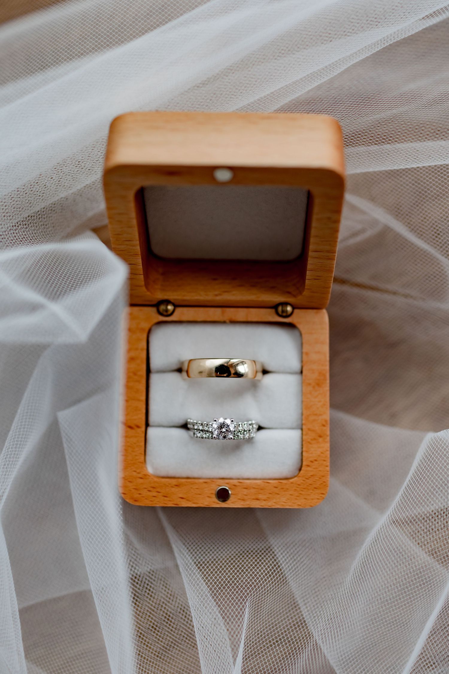 Wedding rings displayed in a wooden box on white tulle fabric, featuring gold and diamond bands.