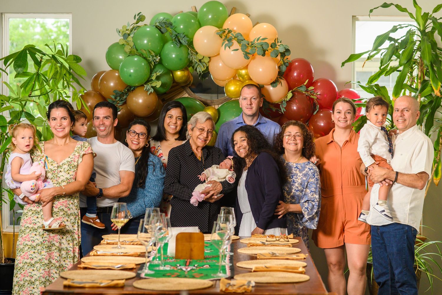 Large multigenerational family group celebrating together indoors with balloon arch decoration.