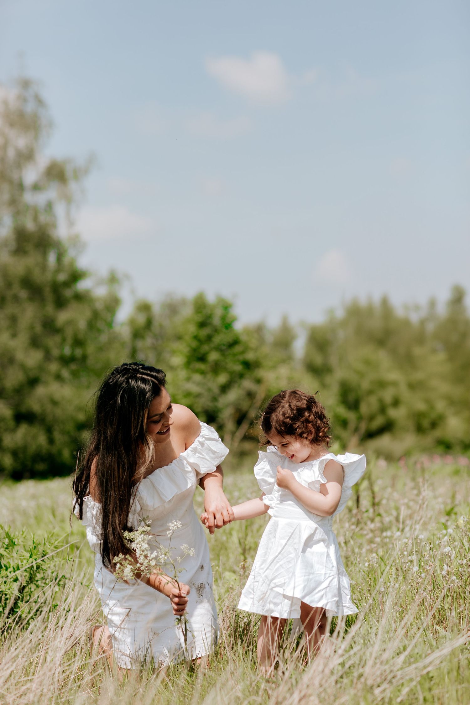 Two people in white dresses exploring a summer meadow together on a bright day.