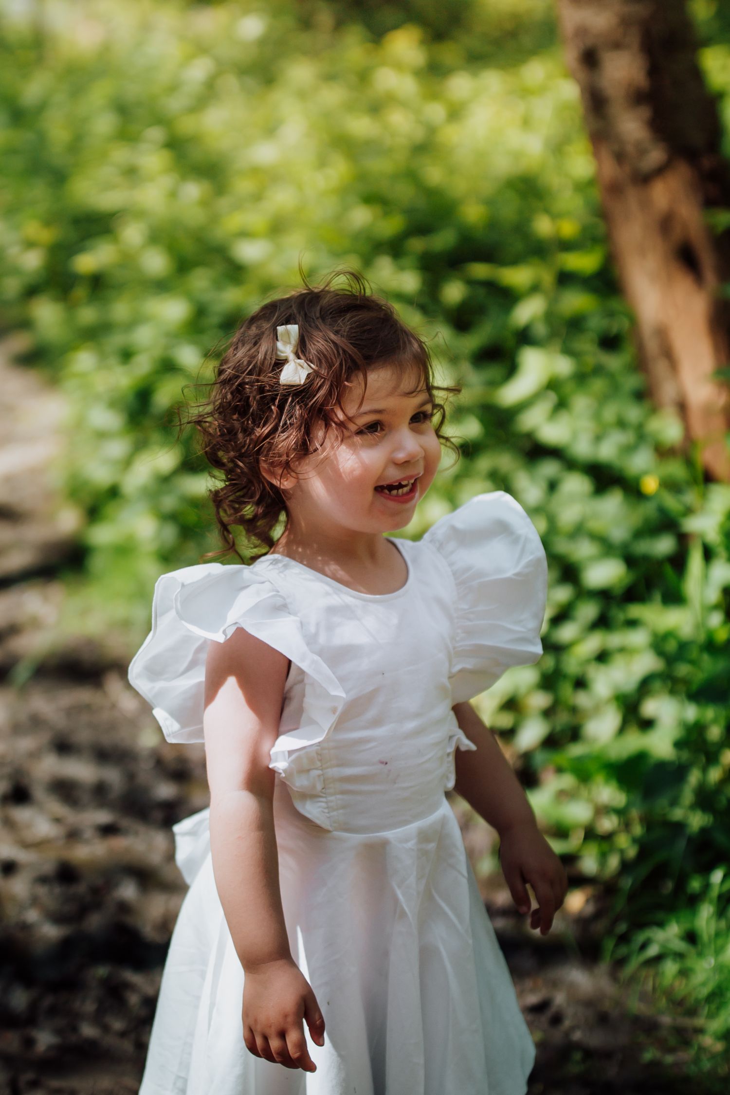 A joyful child in a white puffy dress laughing outdoors in a garden setting.