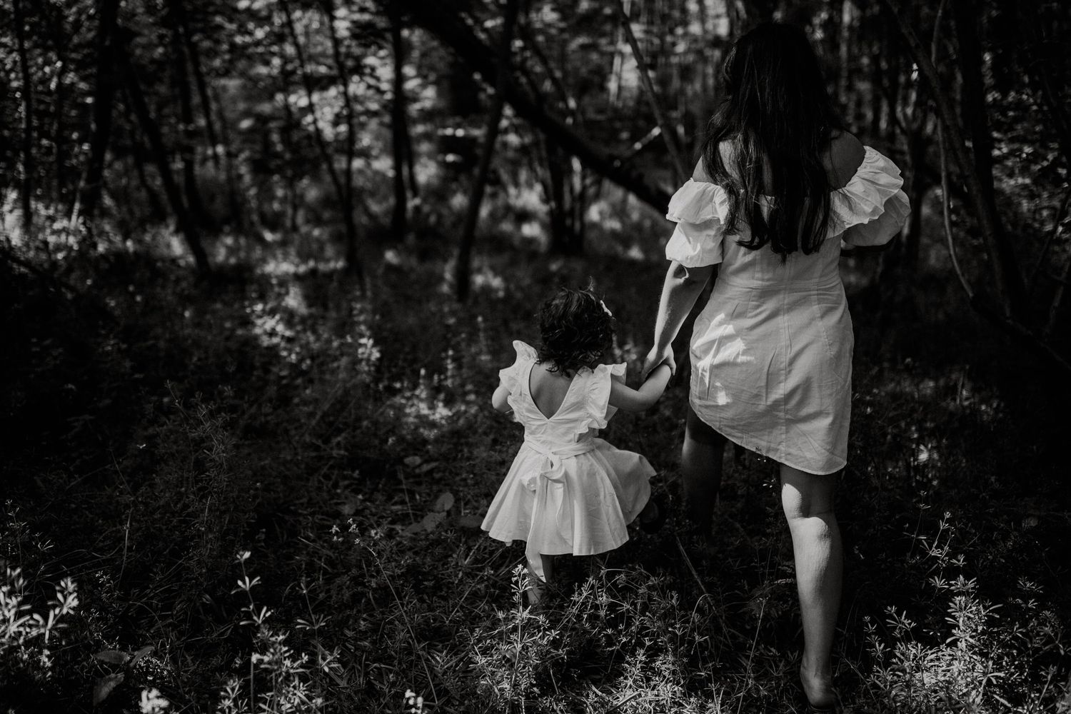 Black and white image of a parent and child holding hands while walking through a dark forest.