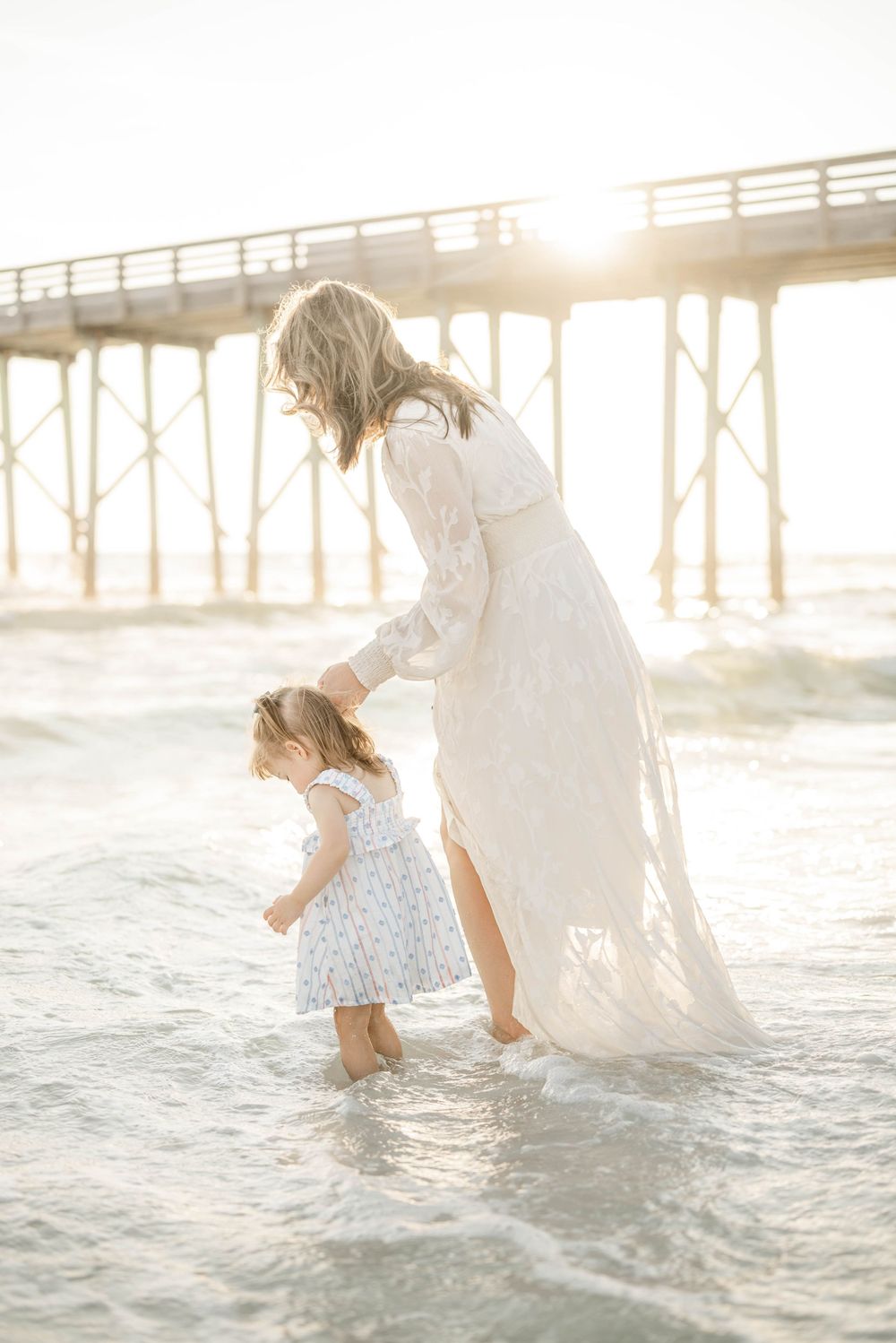 Mother and daughter share a tender moment wading in ocean waves near a pier at sunsetPanama City Beach photographer, family photos PCB, 30A
